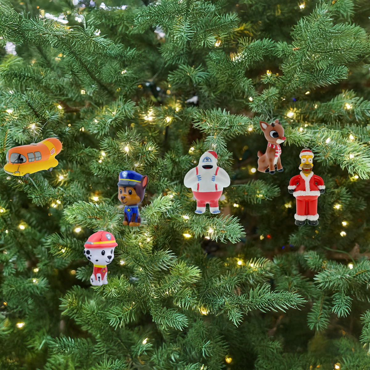 Oscar Mayer Weinermobile ornament, Paw Patrol Marshall and Chase ornaments, Rudolph the Red-Nosed Reindeer and Bumble ornaments, and Home Simpson ornament all hanging on a Christmas tree