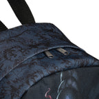 Close-up of the top of a dark charcoal backpack with a subtle black pattern, featuring a zippered pocket with silver metal zippers and a black webbing straps top handle, set against a plain white background.