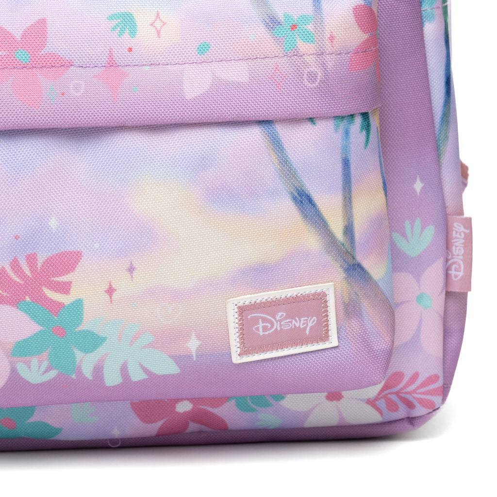 Close-up of a Disney backpack in pastel lavender with a tropical floral and palm tree print, featuring a stitched Disney logo patch on the front.