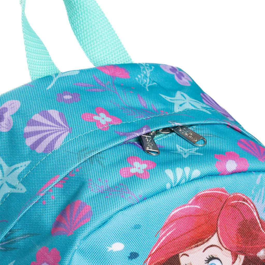 A close-up of a turquoise blue fabric backpack featuring a mermaid-themed print with pink and purple seashells, starfish, floral motifs, and part of a red-haired character illustration. A front zip pocket with silver zipper pulls is visible, along with mint green shoulder straps against a white background.