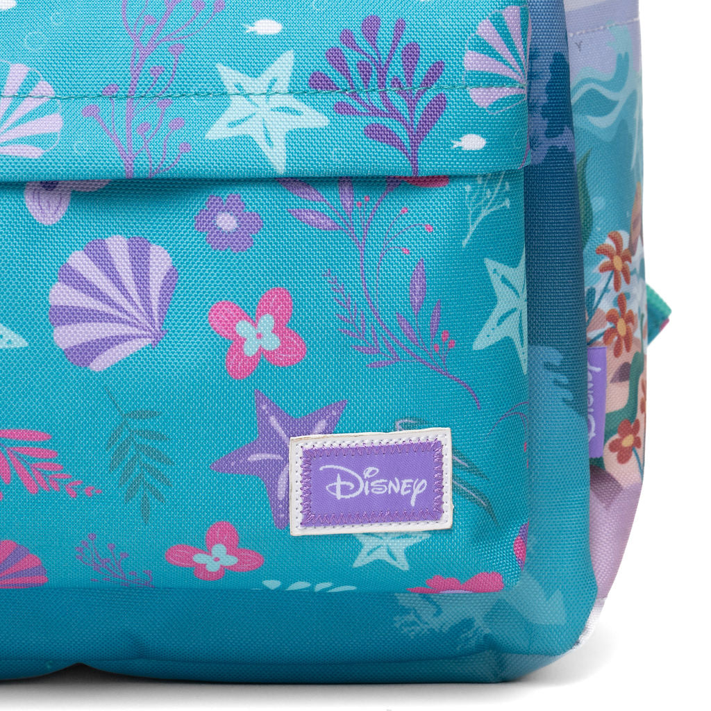 Close-up of a turquoise blue fabric bag with an underwater-themed print featuring purple and pink seashells, starfish, and marine plants. A purple rectangular patch on the front displays the Disney logo.