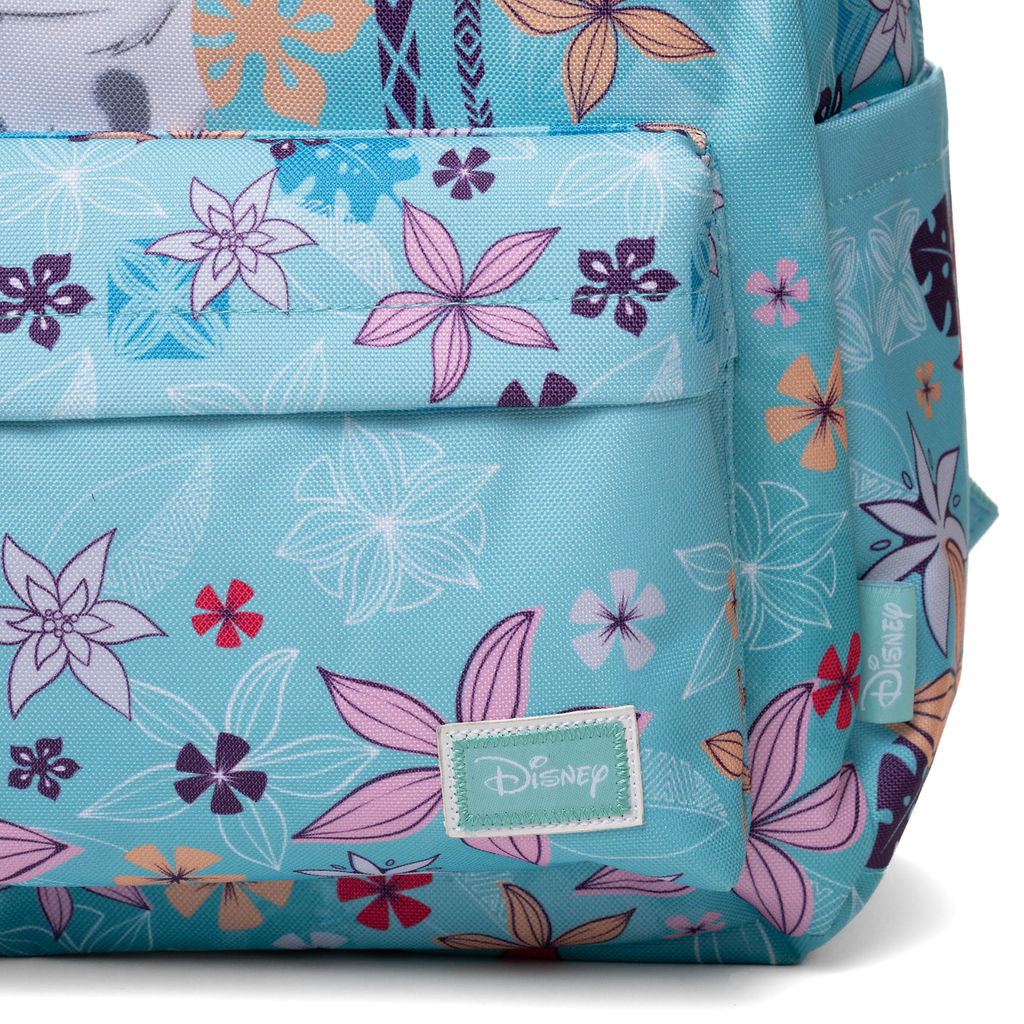 A close-up of a Disney backpack in a light turquoise blue color, decorated with a vibrant floral pattern in pink, purple, orange, and white. The Disney brand name is visible on a stitched patch on the front pocket and on a side tag.