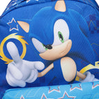 Close-up of a blue backpack featuring Sonic the Hedgehog artwork, with Sonic's face, green eyes, white gloves, and a yellow ring on a patterned blue background.