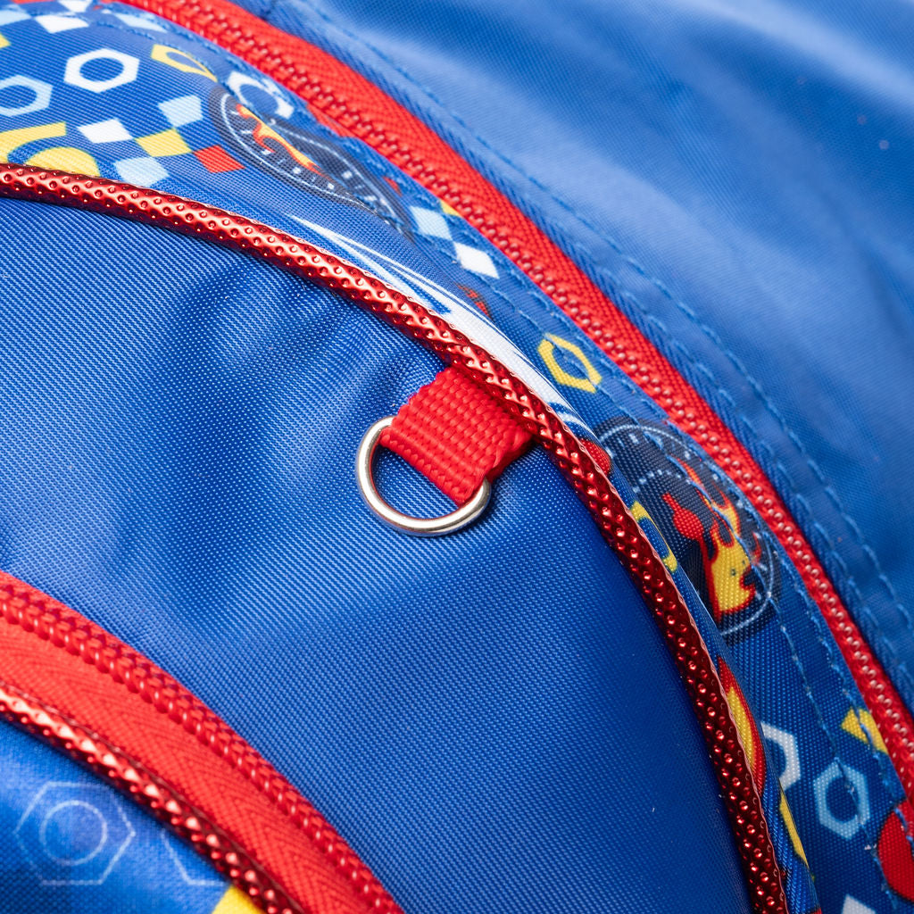 Close-up detail of a blue backpack with red zippers, a red web loop with a metal ring, and a patterned fabric panel featuring nus and bolts and other Cars references.
