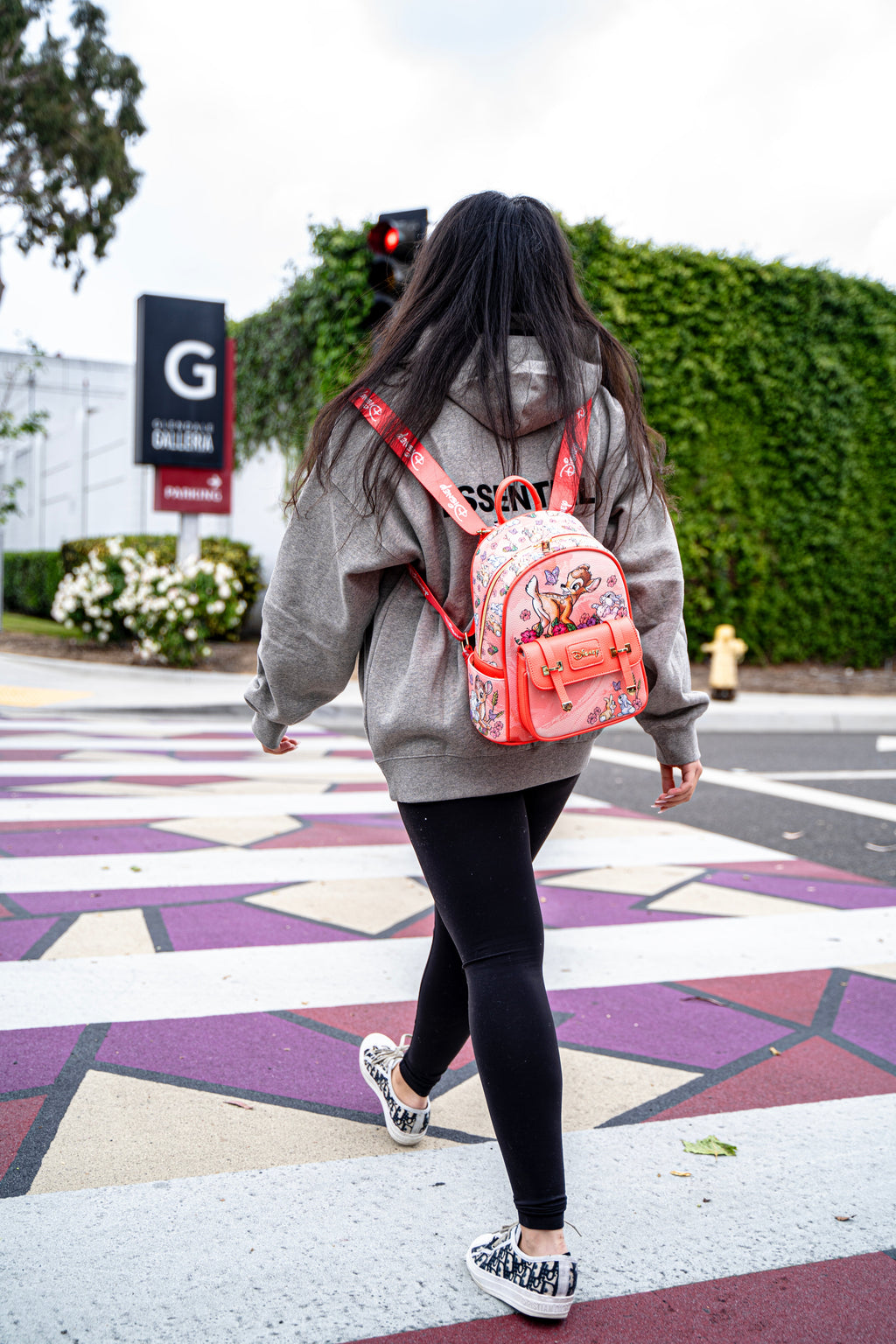 Woman walking across a colorful crosswalk holding a Disney Loungefly Bambi mini backpack