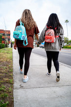 Two women walking hand in hand wearing Disney Loungefly Stitch and Bambi mini backpacks