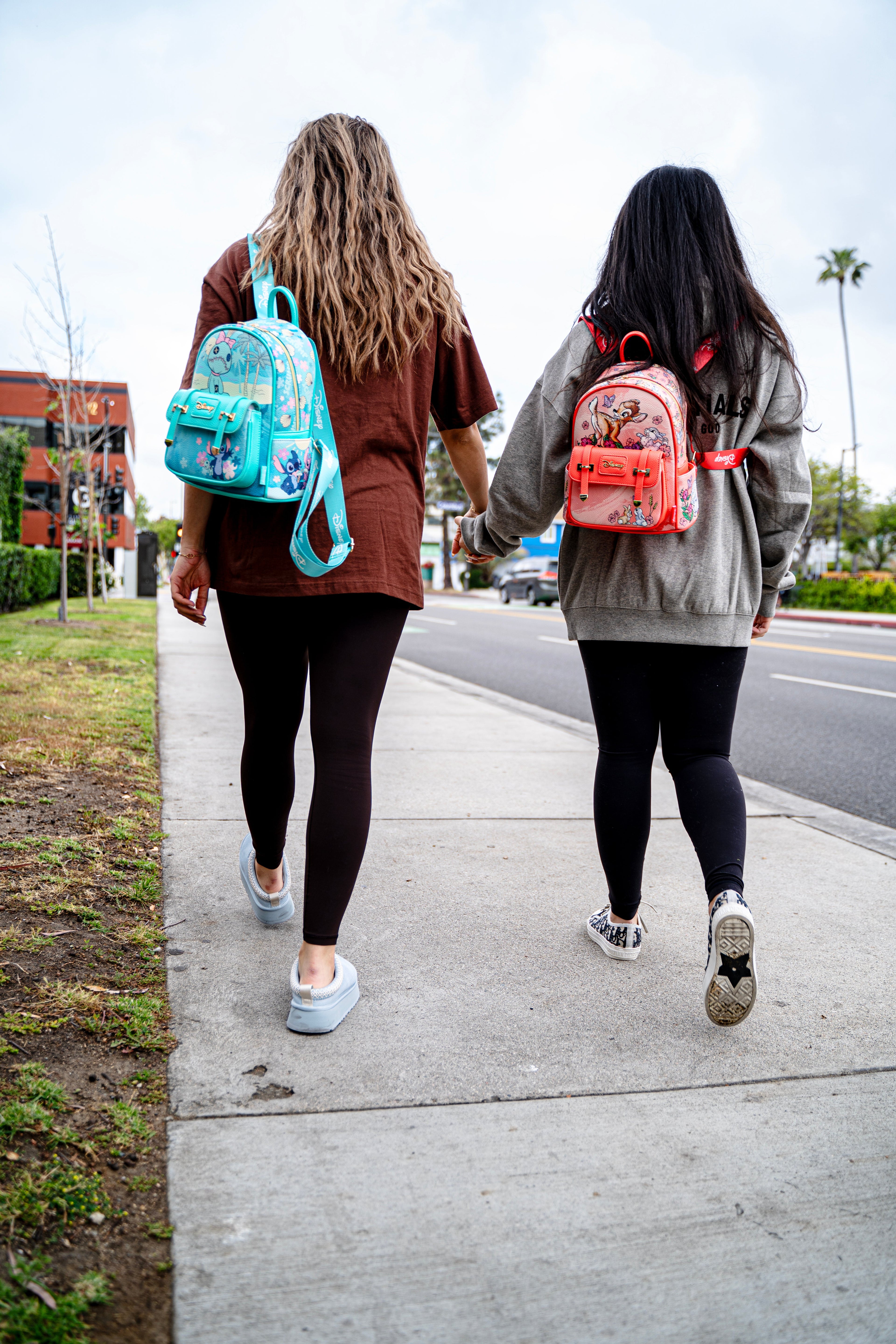 Two women walking hand in hand wearing Disney Loungefly Stitch and Bambi mini backpacks