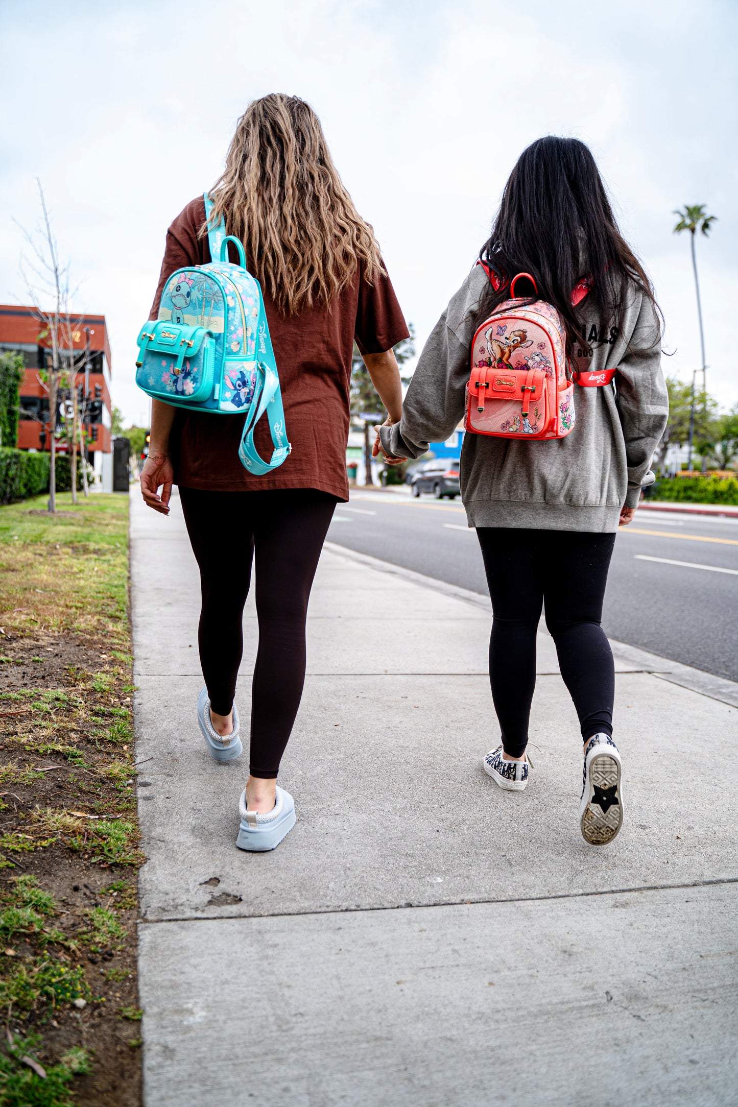 
                  
                    Two women walking hand in hand wearing Disney Loungefly Stitch and Bambi mini backpacks
                  
                