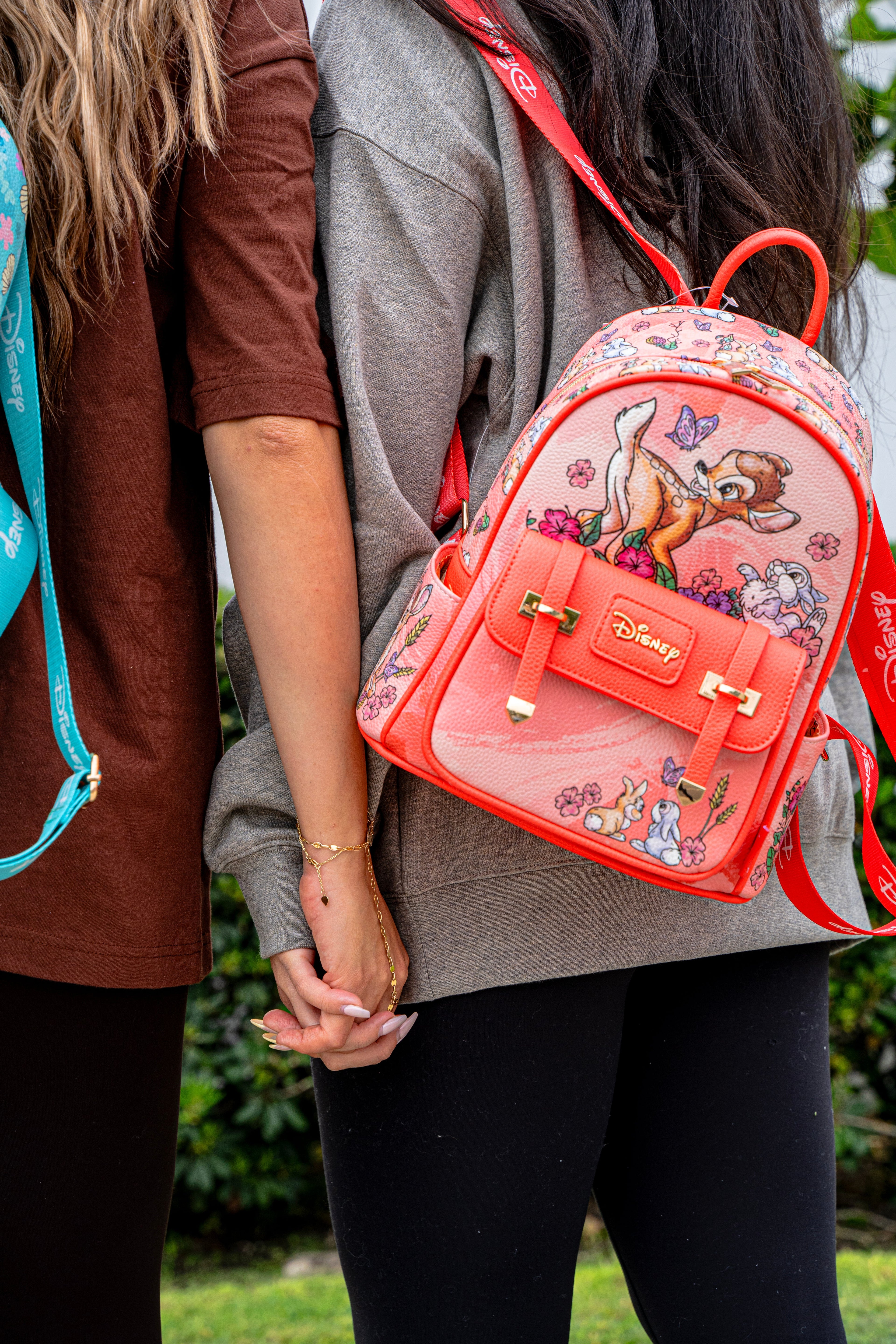 Close-up of two people holding hands while wearing Disney Loungefly mini backpacks featuring Stitch and Bambi