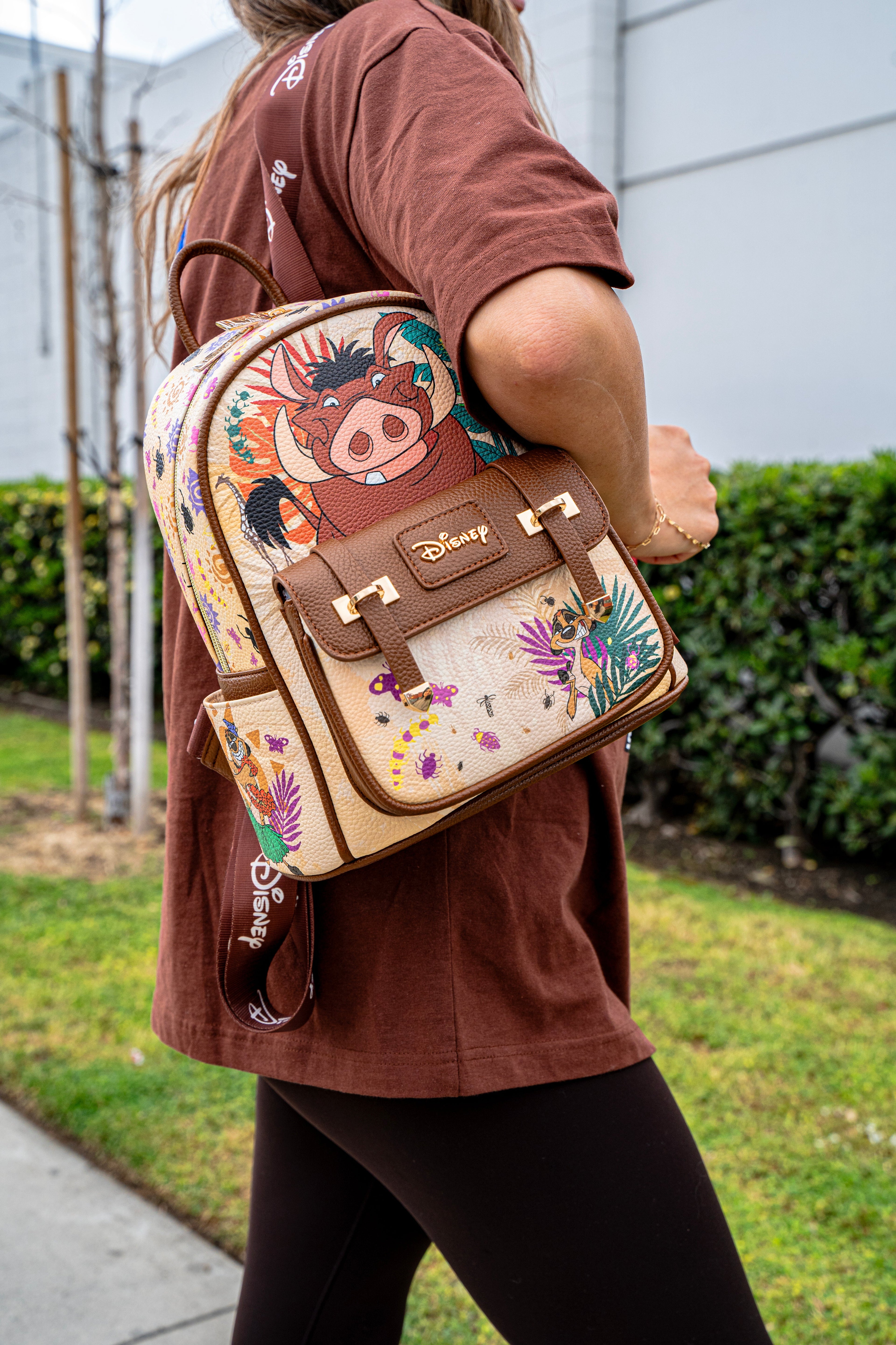 Model wearing a Disney Loungefly Pumbaa backpack from The Lion King collection, outdoors in casual attire.