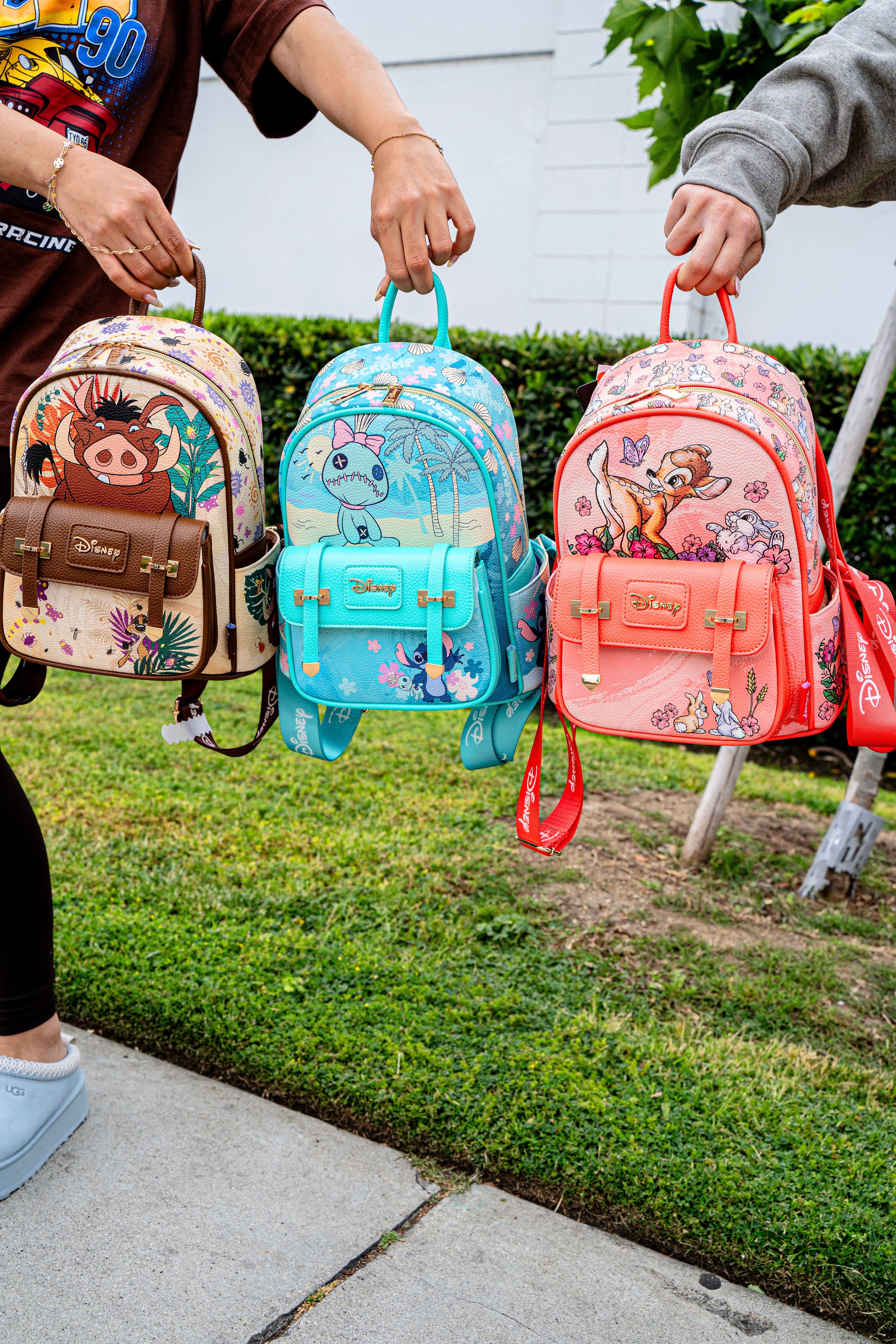 Three Disney Loungefly mini backpacks — Pumbaa, Stitch, and Bambi designs — being held side by side outdoors