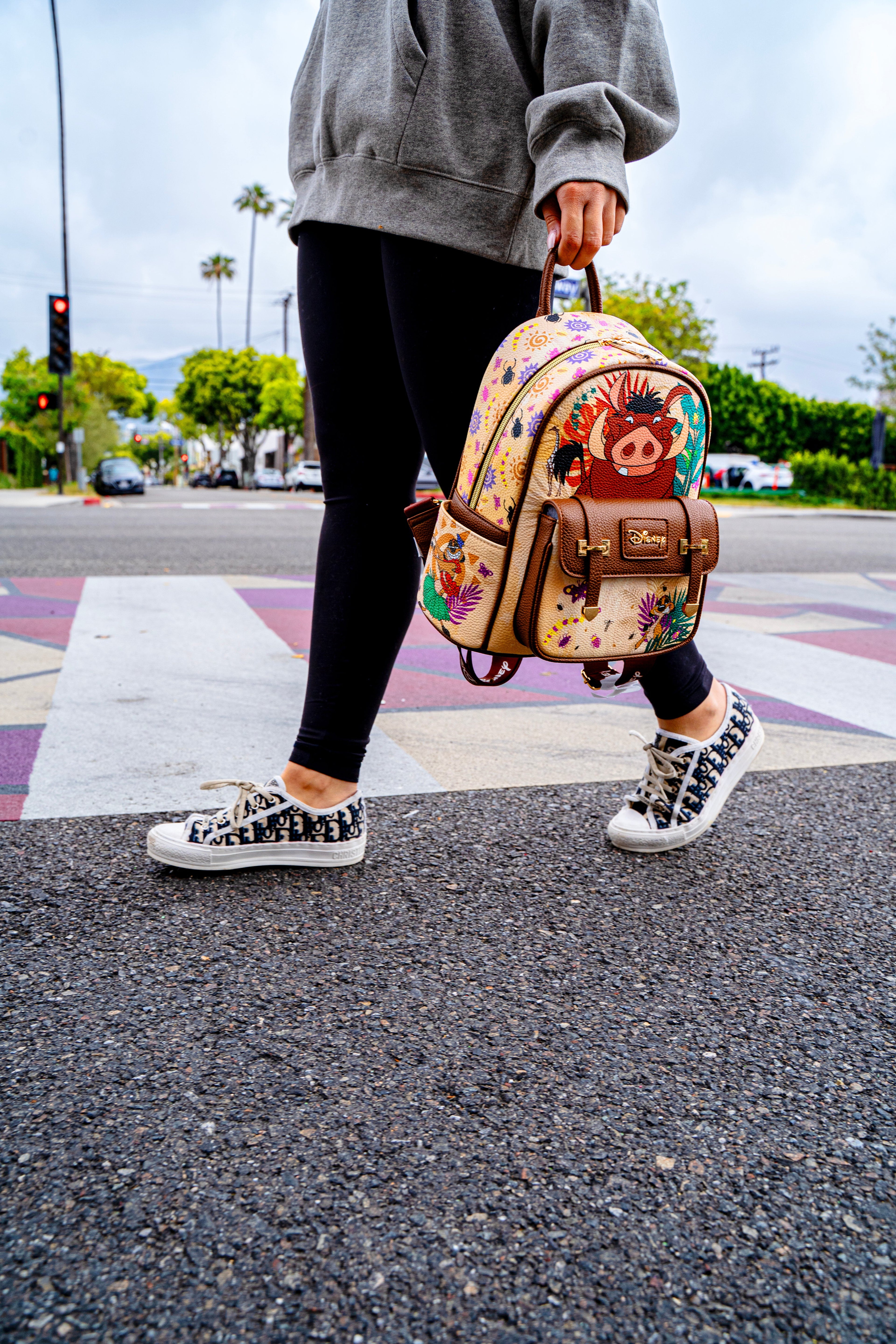 Person crossing the street holding a Disney Loungefly Pumbaa mini backpack from The Lion King collection
